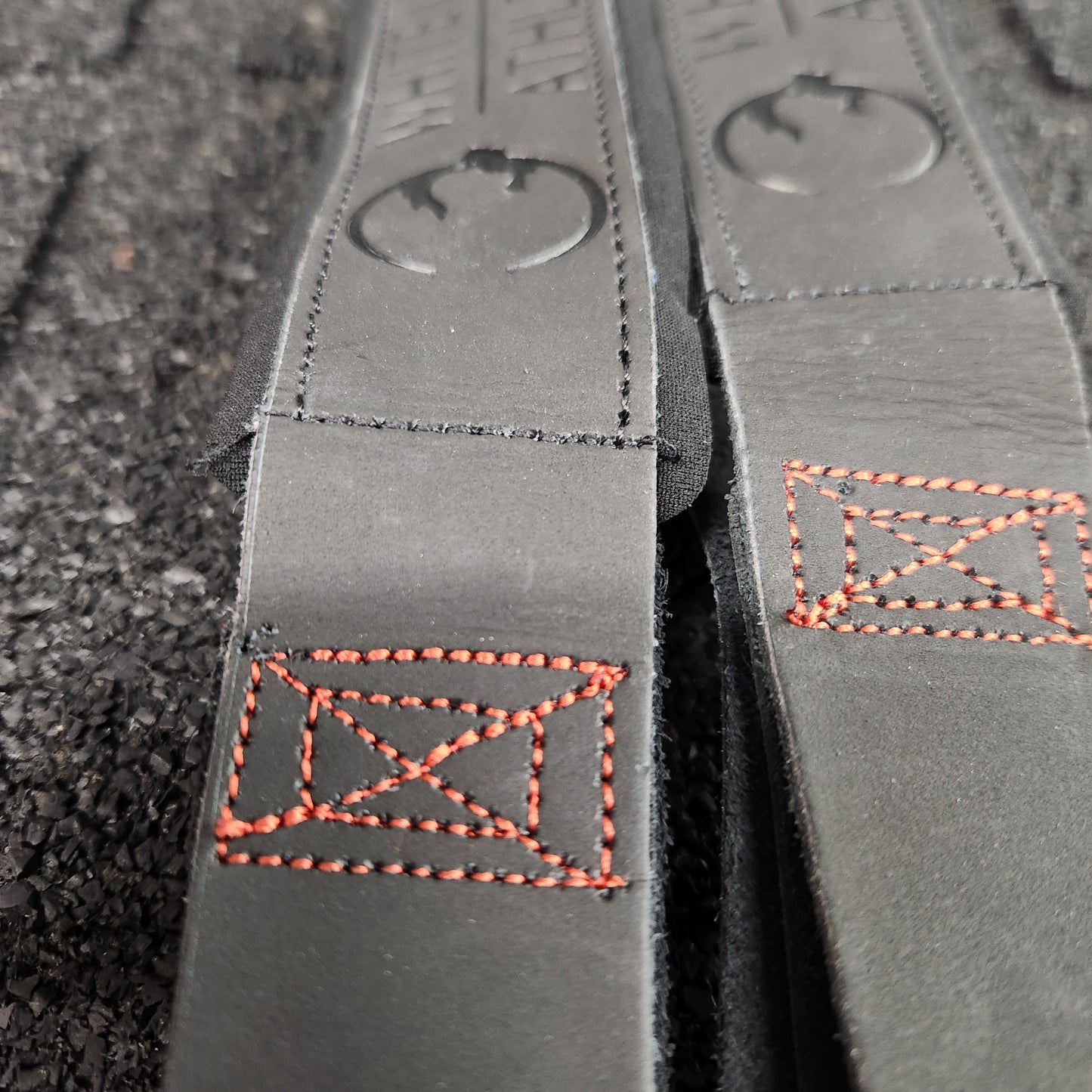 Close-up shot of embossed logo on black leather weightlifting straps by White Lion Athletics.