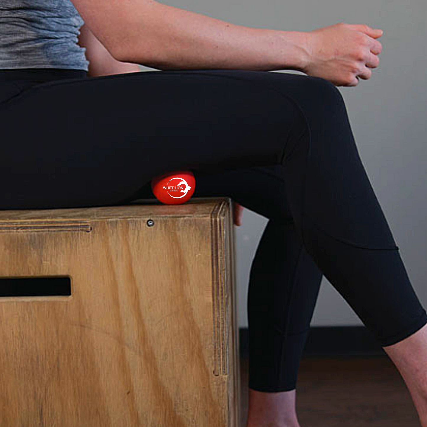 Soft Lacrosse being used for massaging the hamstring while seated on a wooden box.