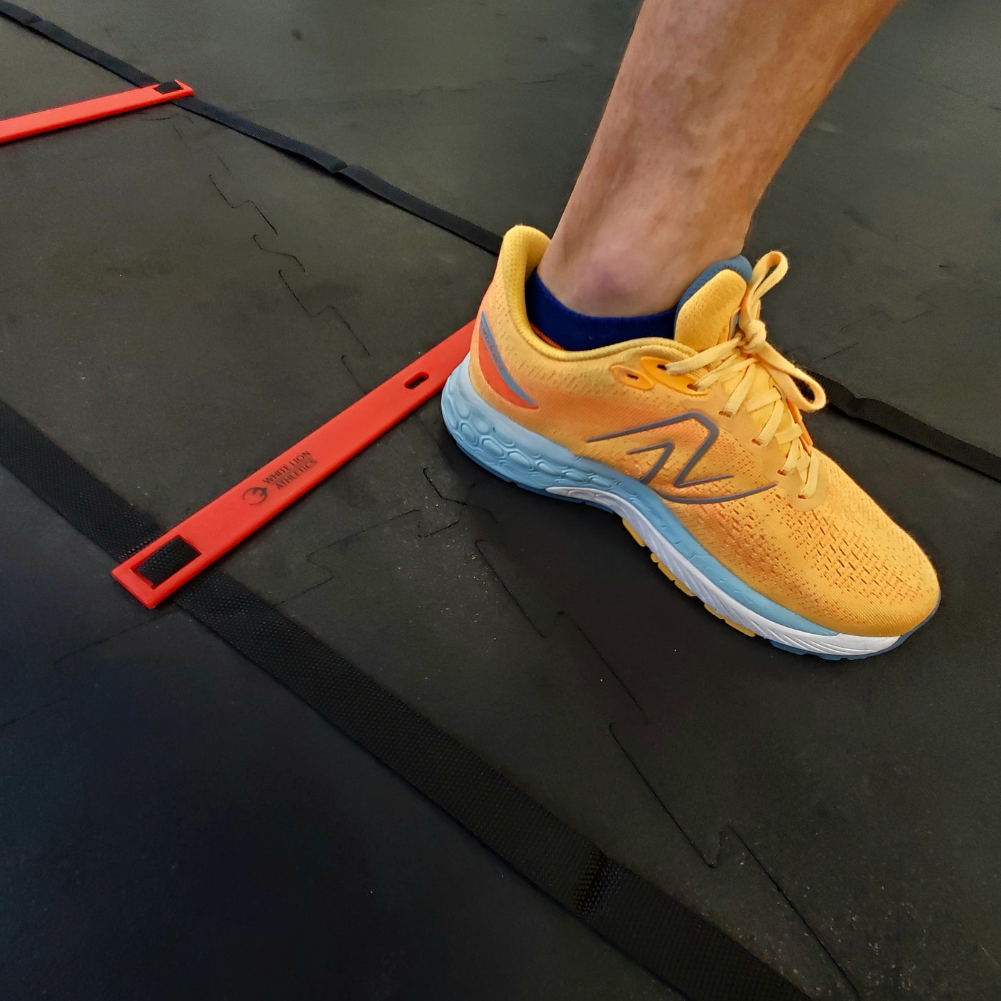 Close-up shot of The left foot of an athlete is shown in the centre of the agility ladder while performing an agility drill with the six metre long White Lion athletics agility ladder