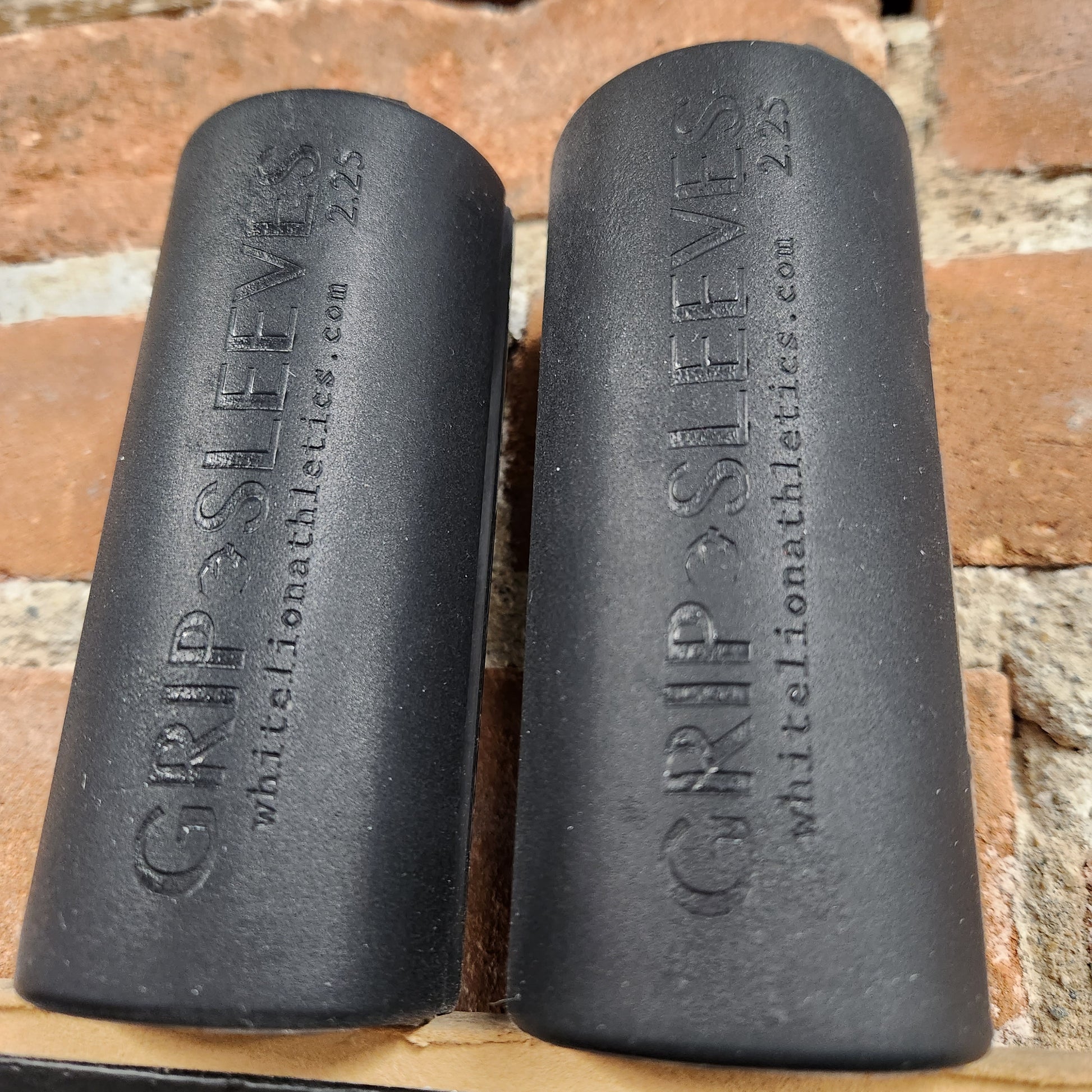 a pair of 2.25" Grip Sleeves by White Lion Athletics displayed against brickwall