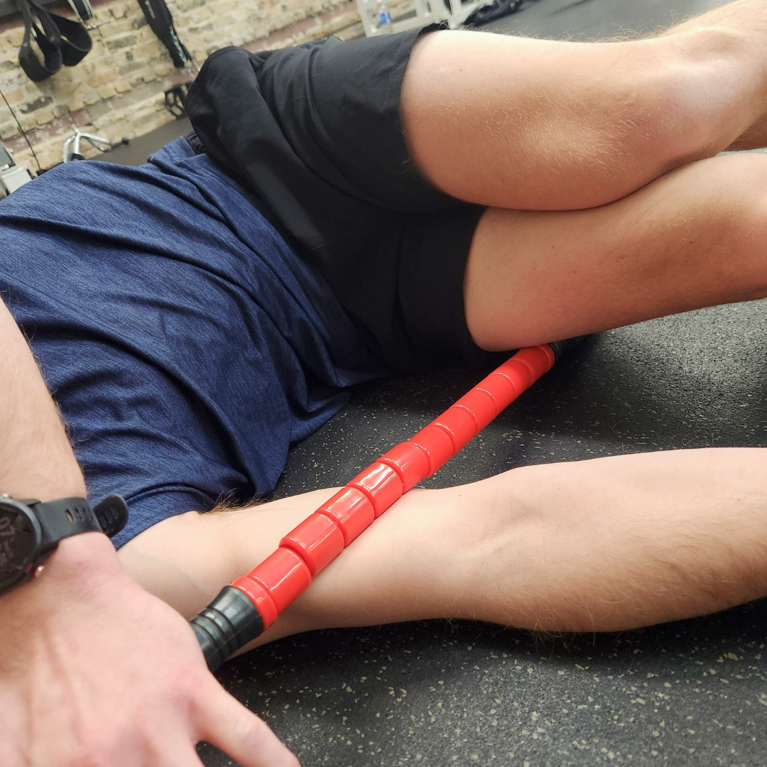 Male athlete using White Lion Athletics Big Red Massage Stick on their right bicep while laying on the ground.